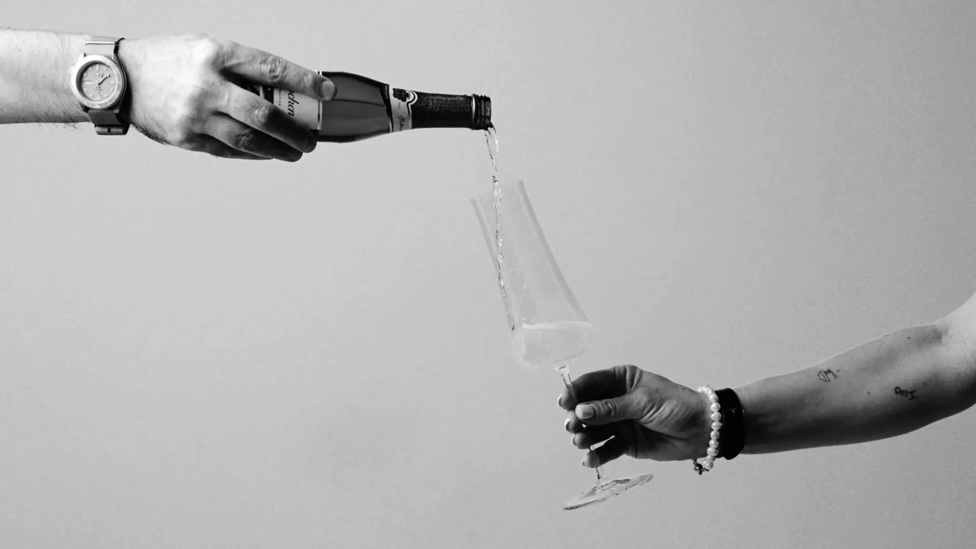 Schwarz-Weiß-Aufnahme, die zeigt, wie Sekt aus einer Flasche in ein Glas gegossen wird.
